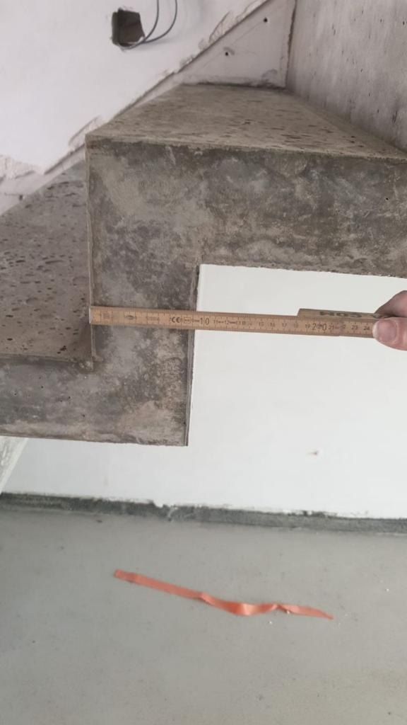 Ein Zollstock liegt an der Kante eines Betonbauteils und nimmt das Maß auf.
